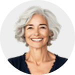 Smiling older woman with short, wavy gray hair, wearing a dark top, posed against a plain light background.